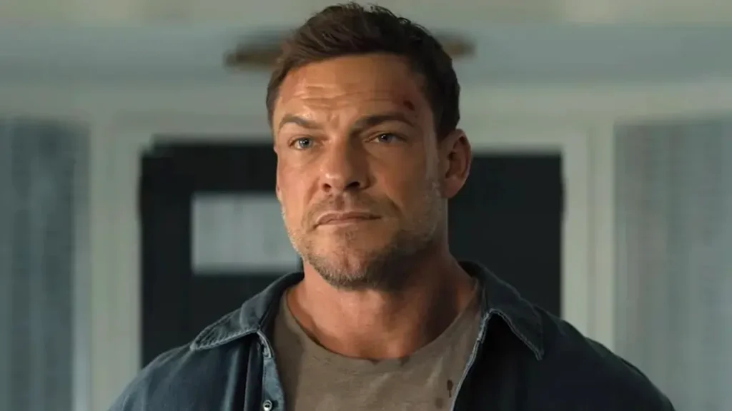 Close-up of Alan Ritchson as Jack Reacher wearing an open denim shirt and looking ahead sternly.